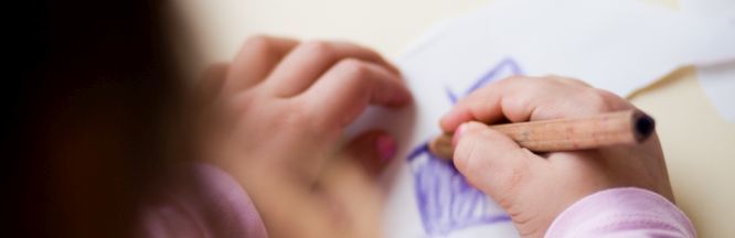 Zu sehen ist der Blick über die Schulter eines Kindes. Das Kind malt mit einem blauen Buntstift.