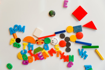 An einer Tafel hängen verschiedene bunte Magnete. Sie stellen Buchstaben, Zahlen, Gesichter und Formen dar.